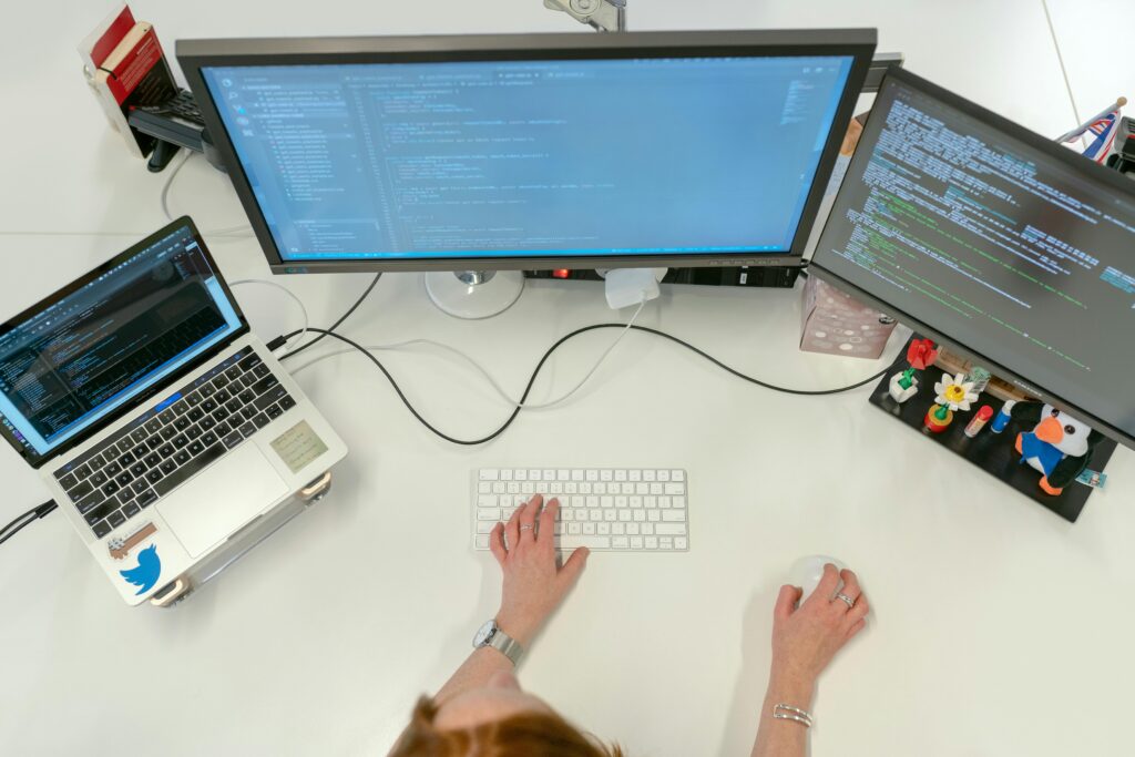 person sitting at desk with laptop and two computer screens